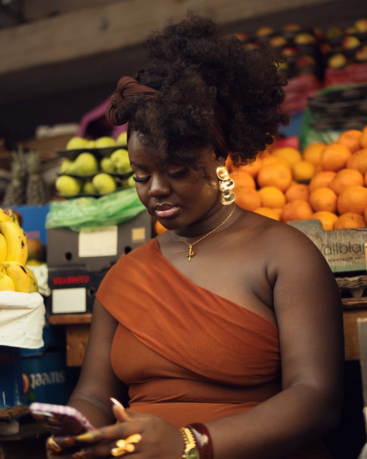 At a market, a customer looks at her phone in front of fruit stalls.